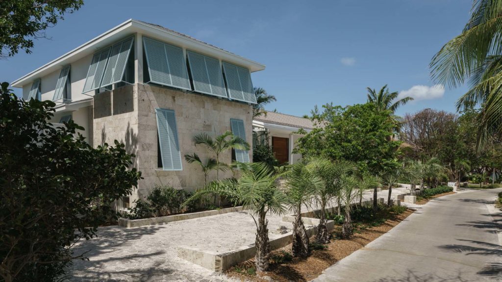 Building Area: 5,000 SF
Building Status: Completed 2018

Inspired by Bahamian architecture, but with a modern twist, this tropical beach house incorporates many of the design and climate adaptations found in traditional Bahamian Architecture. 

The name of the house – “Out of the Blue” came from the client and was inspired by the many layered shades of blue sea which are a hallmark of Cat Cay. The palette of both the architecture and the interiors of the house were inspired by nature and our desire to connect to the beauty all around. Most of the house has a soft palette of natural and made materials – concrete, Cuban tiles, light wood. The restful white and soft blues of the walls serve both as respite and contrast to the vivid colors of the tropical seas and gardens outdoors.

The house includes Bahamian shutters, porches, breezeways, native keystone, and volume ceilings with wood cladding –elements with deep roots in Bahamian vernacular. The modern feel of the house is expressed in the openness of the Great Room, the immediacy of the connection to the dramatic reflecting pool outdoors, and the simple concrete decks perched above the rocks and beach below. Sliding doors in the main space retract to allow for 20 feet of gorgeous, uninterrupted ocean views.

The Bahamian roots of the house also provide several important resiliency features: cross ventilation makes public spaces well ventilated and AC optional during much of the year. Elevated decks capture the breezes and shady porches block the sun. The mechanical and electrical is lifted from the grounds and incorporated into the architecture. The basement houses several large water cisterns that capture the water from the gutters and pitched roofs.
 
The materials are simple to maintain in a harsh marine environment and unfussy. This is a tropical beach house designed to be enjoyed with family and friends.